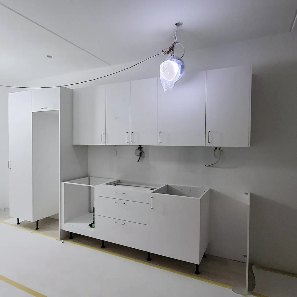 Montering av vitt kök med väggskåp och bänkskåp under renovering i Bjurbäcken